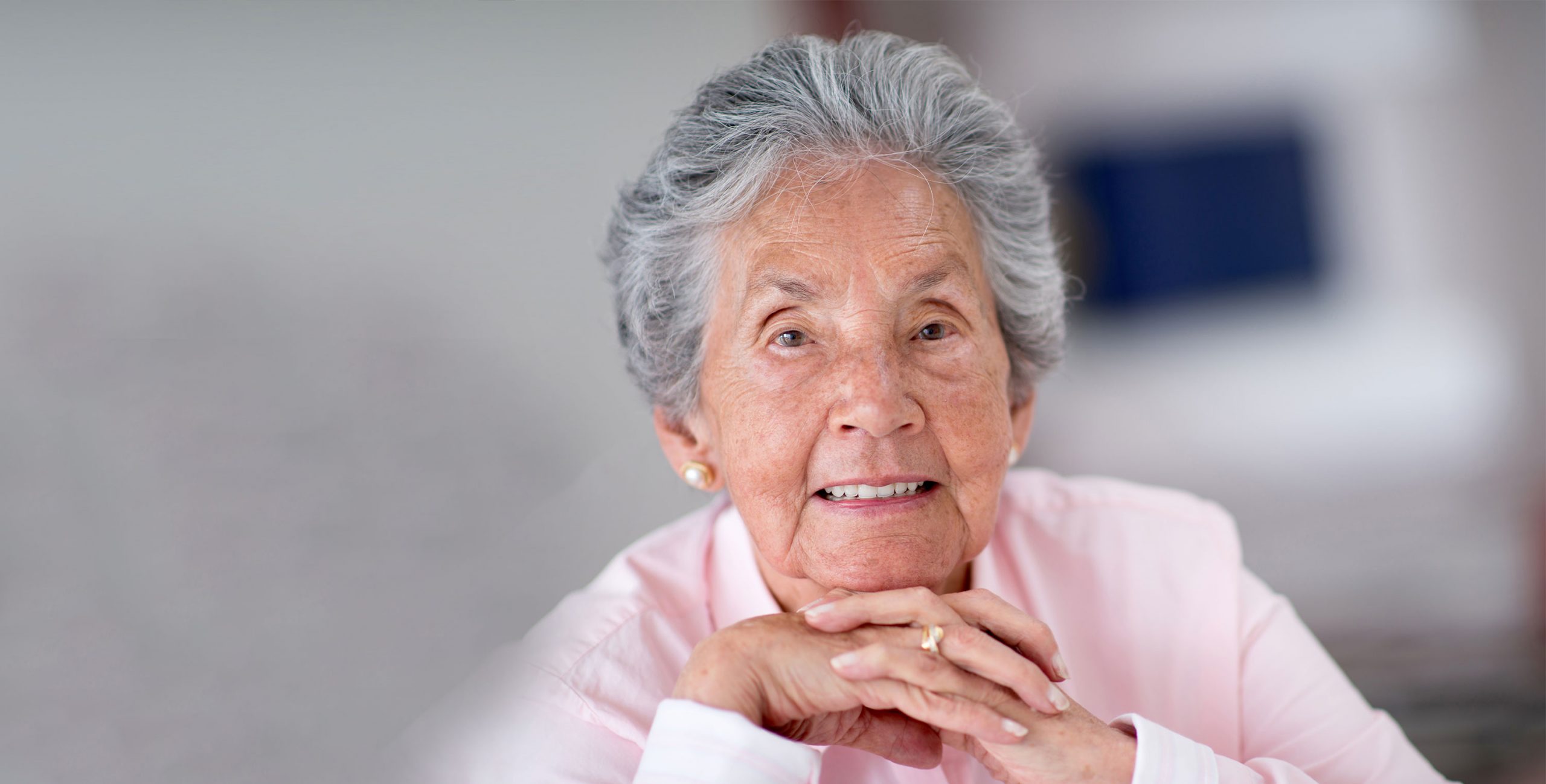 A photo of a mature lady wearing pink and holding her hands under her chin