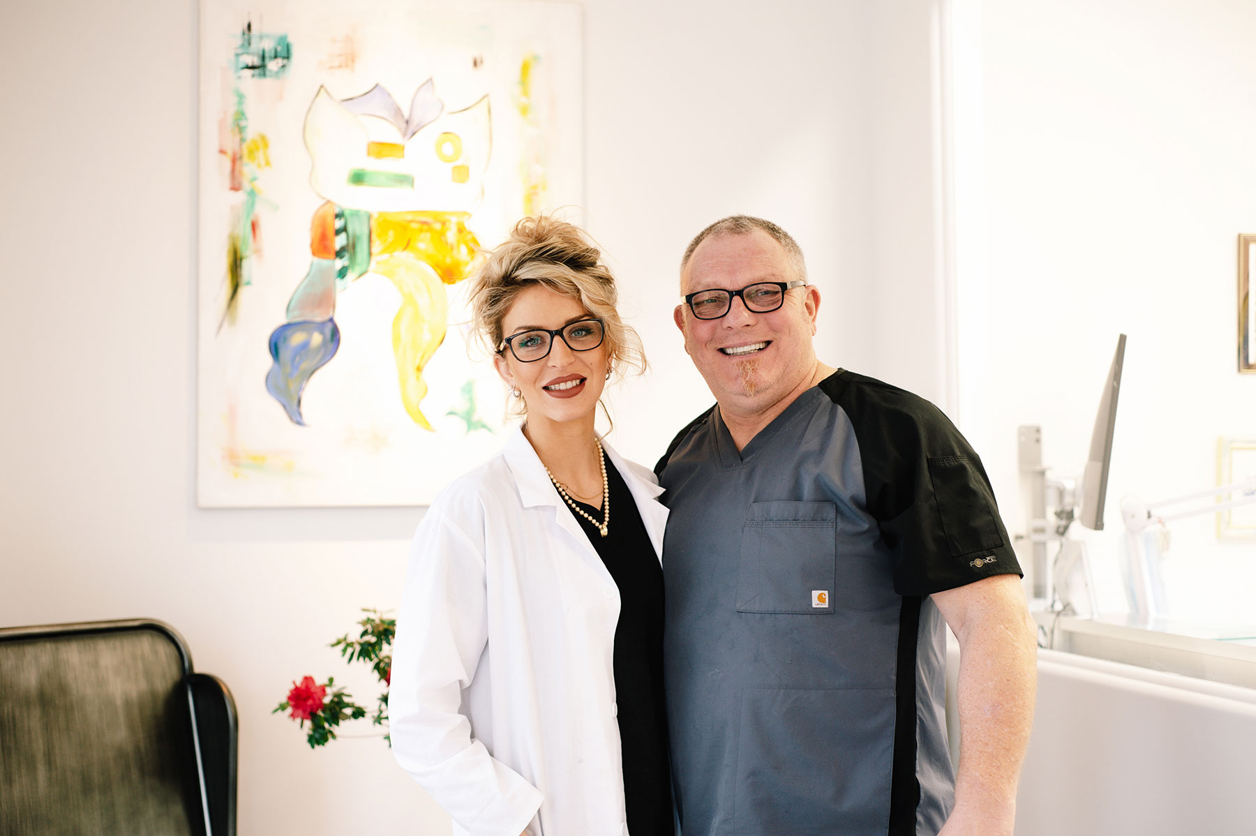 The denturist and the master ceramist posing for a photo in front of a wal with a medical diagram